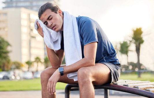 Athlete deciding should you work out when tired, sitting on gym floor with head in hands looking exhausted